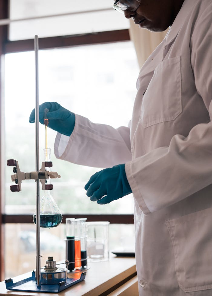 creative-01 Side view of concentrated African American scientist in protective goggles and latex gloves examining chemistry substance in flask while working with modern equipment in laboratory