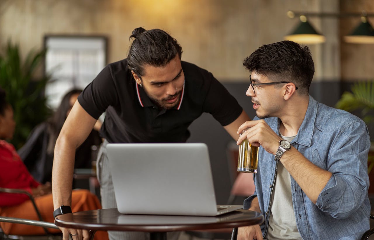 brand-02 Men having a relaxed conversation over drinks and laptop in a cozy café setting.