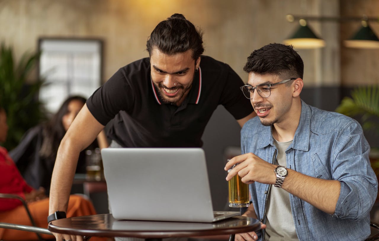 brand-01 Two men enjoying a casual meeting in a cafe, sharing laughs and drinks over a laptop.